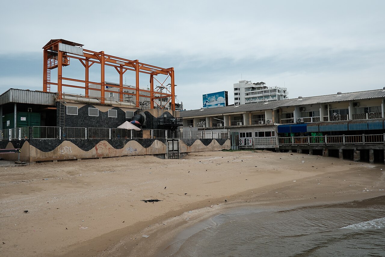 DSCF0718 Empty sandy beach in front of a row of seaside buildings and an orange steel stru