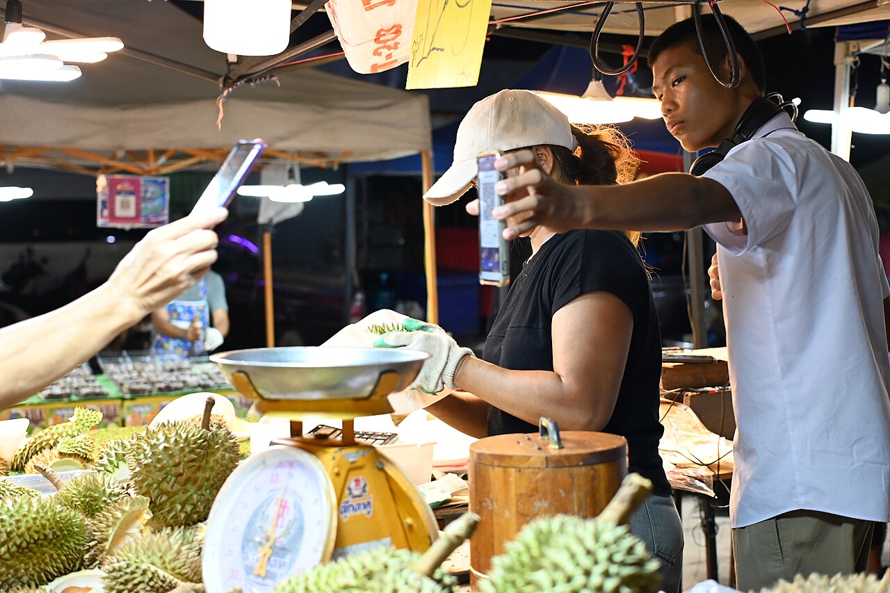 DZ3 0627 A night market stall in Sattahip Thailand - vendors weigh durians as a young buye